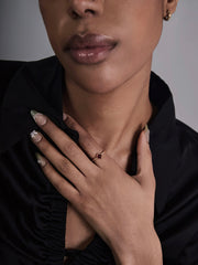 A person touches their chest, showcasing manicured nails with white floral designs and the CAMELLIA 14K Solid Gold Carena Garnet Ring while wearing a black collared shirt.