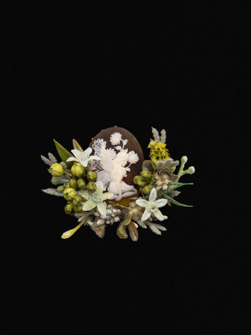 The Peony Birth Flower Ring by CAMELLIA, crafted in New York, showcases an ivory cameo with a fairy surrounded by preserved flowers and foliage on a black background. The Peony Birth Flower Ring by CAMELLIA, crafted in New York, showcases an ivory cameo with a fairy surrounded by preserved flowers and foliage on a black background.