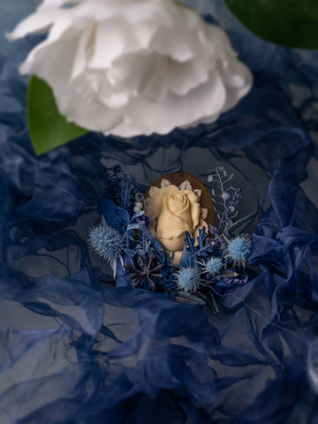 A white rose adorns a decorative dessert, accented by blue flowers and fabric. In the foreground, a large white flower mirrors the elegance of CAMELLIA's exquisite Camellia Birth Flower Ring, echoing the beauty of handcrafted jewelry. A white rose adorns a decorative dessert, accented by blue flowers and fabric. In the foreground, a large white flower mirrors the elegance of CAMELLIA's exquisite Camellia Birth Flower Ring, echoing the beauty of handcrafted jewelry.