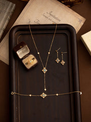 The CAMELLIA Aurielle Opal Jewelry Set, featuring a necklace, bracelet, earrings, and ring in a box, elegantly rests on a wooden tray. This hypoallergenic collection blends timeless design with exquisite gemstones for sensitive skin.