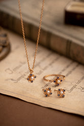 The Chloe Pearl Tanzanite Jewelry Set by CAMELLIA features a stunning yellow gold necklace, ring, and earrings with pearl and tanzanite accents, elegantly showcased on vintage paper with a softly blurred book in the background.