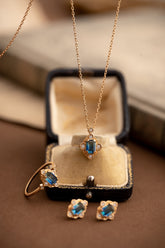 The Louisa Sapphire Jewelry Set by CAMELLIA features a stunning collection of gold jewelry, including a necklace, ring, and earrings displayed elegantly on a vintage jewelry box.