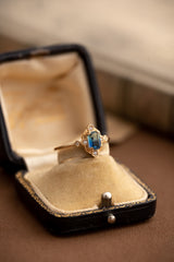 The Louisa Sapphire Jewelry Set by CAMELLIA features a gold ring with a rectangular sapphire gemstone and small side stones, elegantly displayed in an open black and cream box.