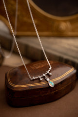 The CAMELLIA Starlight Opal Jewelry Set features a handcrafted sterling silver necklace with star-shaped links and an opal pendant, elegantly displayed on a closed brown leather box.