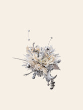 This exquisite floral arrangement, featuring silver and white blooms, metallic spheres, and decorative charms, mirrors the elegance of CAMELLIA's Moon Flower Ring against a plain backdrop.