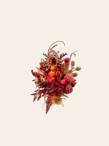 The Sun Flower Ring by CAMELLIA features a handcrafted decorative cluster of red and orange dried flowers with a circular jewel centerpiece, designed in New York, all set against a light background. The Sun Flower Ring by CAMELLIA features a handcrafted decorative cluster of red and orange dried flowers with a circular jewel centerpiece, designed in New York, all set against a light background.