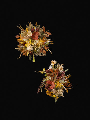 Two Free Poetic Boho Wedding Flower Rings by CAMELLIA feature clusters of assorted dried and artificial flowers with yellow, orange, and brown hues, arranged on a plain black background. Two Free Poetic Boho Wedding Flower Rings by CAMELLIA feature clusters of assorted dried and artificial flowers with yellow, orange, and brown hues, arranged on a plain black background.