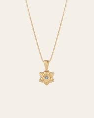 The CAMELLIA Elsa Cherry Aquamarine Necklace, a handcrafted gold piece with a star-shaped pendant and a central blue gemstone, elegantly displayed on a light background, radiates charm and sophistication.