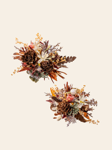 Two Vintage Maillard Modern Year Wedding Flower Rings by CAMELLIA, featuring pine cones, dried leaves, and small yellow flowers on a light background, reminiscent of rustic floral arrangements. Two Vintage Maillard Modern Year Wedding Flower Rings by CAMELLIA, featuring pine cones, dried leaves, and small yellow flowers on a light background, reminiscent of rustic floral arrangements.