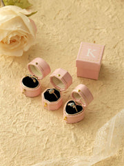 Three CAMELLIA Customized Vintage Ring Boxes with gold clasps, each showcasing a unique ring, are arranged on a textured beige surface near a rose and lace-trimmed fabric.