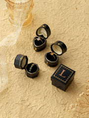 Four Customized Vintage Ring Boxes by CAMELLIA rest on a textured surface, three open to display gold rings and a necklace, one closed with an "L" monogram. Lace and dried flowers are placed nearby.