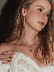 A woman with wavy light brown hair wears a white lace top, CAMELLIA Cámellia Mother of Pearl Necklace, and natural makeup, looking off to the side with a neutral expression.