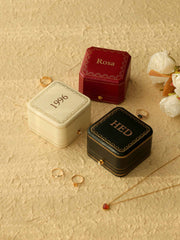 Three CAMELLIA Customized Vintage Jewelry Boxes, each embossed with "Rosa," "1996," and "HED," rest on a textured surface, accompanied by rings, a necklace, and white roses.