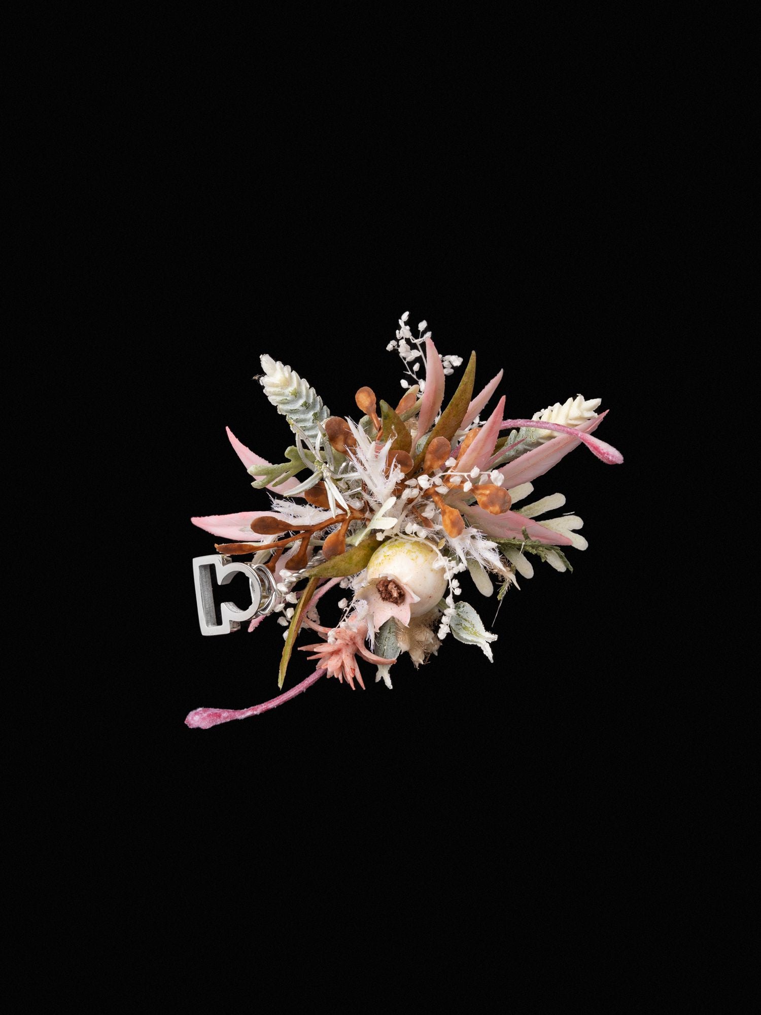 The CAMELLIA Libra Flower Ring features a handcrafted skull and crossbones design using pink and white flowers with lush greenery on a black background.