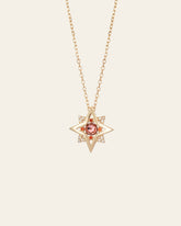 The CAMELLIA New York Garnet Pentagram Necklace is a handcrafted gold star-shaped pendant featuring a central garnet gemstone, encircled by sparkling clear stones on a fine sterling silver chain.