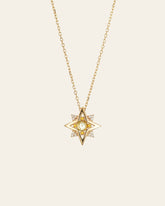 The CAMELLIA New York Peridot Pentagram Necklace is a gold piece featuring a star-shaped pendant with a central peridot gemstone and diamonds, set against a light background.