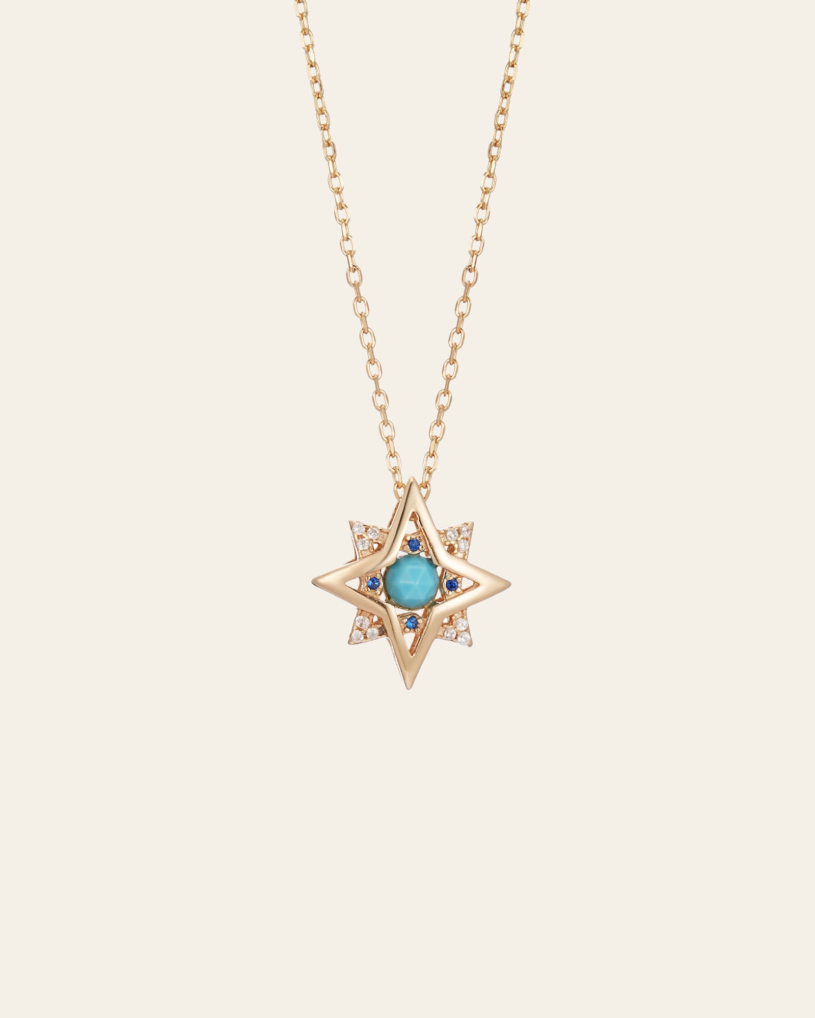 The New York Turquoise Pentagram Necklace by CAMELLIA is a handcrafted gold chain piece with a star-shaped pendant, central turquoise stone, and small clear stones at the tips.