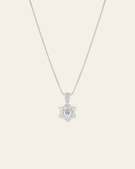 Introducing the Elsa Cherry Aquamarine Necklace by CAMELLIA: a meticulously handcrafted silver chain adorned with a flower-shaped pendant featuring a small aquamarine gem at its center.