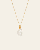 The Alyssa Barquoe Pearl Necklace by CAMELLIA features a gold chain with a single large, irregular white pearl pendant. With its 14K gold vermeil finish, it exudes timeless elegance and evokes French vintage design against a plain background.