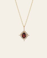 The Claire Garnet Diamond Necklace by CAMELLIA showcases a stunning round red garnet pendant, adorned with diamond accents, elegantly suspended from a gold chain.