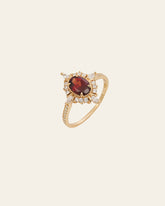 The Claire Garnet Diamond Ring by CAMELLIA is a breathtaking vintage piece. It showcases an oval red garnet at the center, surrounded by small clear stones in a floral design, making it a perfect and timelessly elegant choice for an engagement ring.