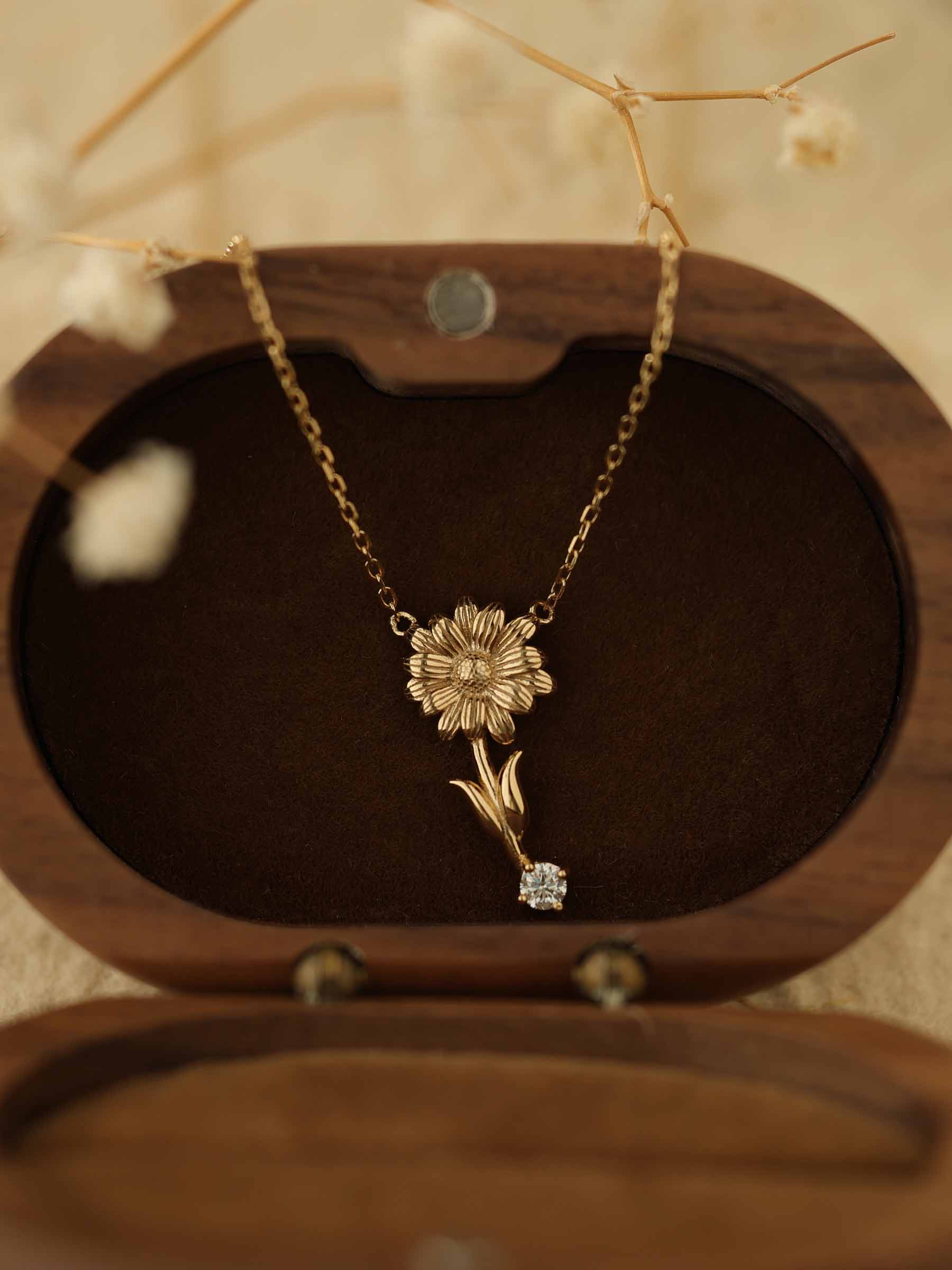 The Nerissa Daisy Diamond Necklace, by CAMELLIA, features a floral pendant with a gemstone in hypoallergenic 14K Yellow Gold Vermeil. It's elegantly presented in an oval wooden box lined with dark velvet and accented by dried flowers for lasting beauty.