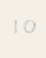 Displayed against a plain beige background, the 15mm Mother Hoops by CAMELLIA showcase their smooth, simple design. One earring is shown from the side and the other from the front, highlighting their elegance. Crafted in sterling silver to be hypoallergenic, they offer everyday comfort.