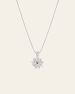 The Elsa Lotus Ruby Necklace by CAMELLIA is a sterling silver piece with a lotus pendant featuring a central pink gemstone. Handcrafted in New York, it embodies elegance and artistry against its plain light backdrop.