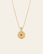 The Elsa Peony Sapphire Necklace by CAMELLIA features a sunflower-shaped pendant with a central blue gemstone, set in 14K yellow gold vermeil. Designed to be hypoallergenic, it's ideal for those with sensitive skin.