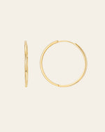Displayed against a plain off-white background, the 40mm Mother Hoops by CAMELLIA are two gold hoop earrings made from 14K Yellow Gold Vermeil and hypoallergenic nickel-free materials. One earring highlights an elegant side view, while the other showcases its full circular shape.