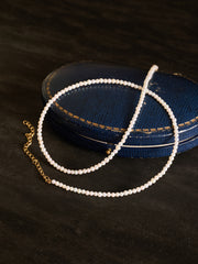 The CAMELLIA Classic Pearl Strand Necklace, featuring a gold chain clasp, is elegantly coiled on a blue oval jewelry case against a dark background, highlighting the timeless beauty of this refined piece.