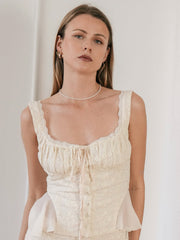 A woman with long hair wears a sleeveless, buttoned ivory dress with lace trim against a plain background. She elegantly accessorizes with CAMELLIA's 3mm Pearl Chain Necklace in 14K Yellow Gold Vermeil, adding a luxurious touch to her timeless look.