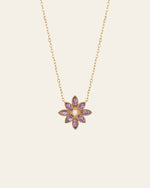 The Cámellia Amethyst Pearl Necklace by CAMELLIA features shimmering amethyst gemstones and a central yellow gem in a flower-shaped pendant crafted from 14K Yellow Gold Vermeil, set against a light background.