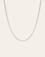 The Tennis Chain Necklace by CAMELLIA, crafted with evenly spaced small square links in sterling silver, is elegantly displayed against a plain, light backdrop.