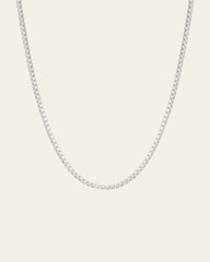 The Tennis Chain Necklace by CAMELLIA, crafted with evenly spaced small square links in sterling silver, is elegantly displayed against a plain, light backdrop.