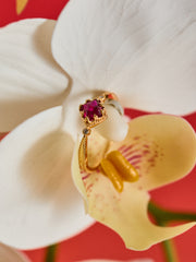 The Carena Ruby Ring by CAMELLIA, featuring a vintage floral design and red gemstone, is displayed on a white orchid petal against a vibrant red background.