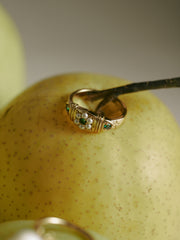 The CAMELLIA Charlotte Pearl Emerald Ring, featuring vintage-inspired gold vermeil with pearl and green gemstone accents, is displayed on a speckled yellow apple beside a thin branch.
