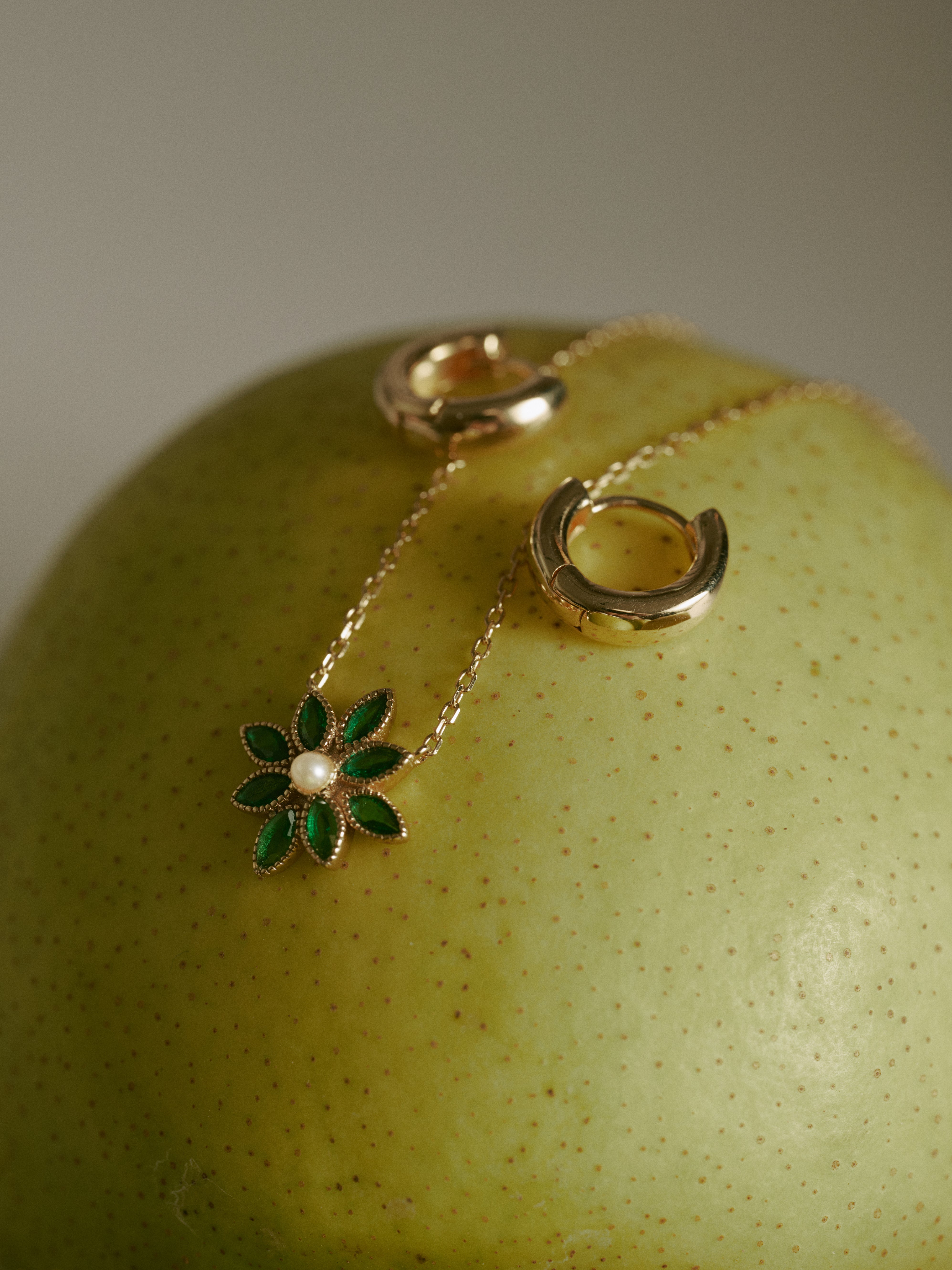 CAMELLIA’s Mia Hoops and a 14K gold vermeil necklace with a green flower pendant are elegantly displayed on a fresh green apple.