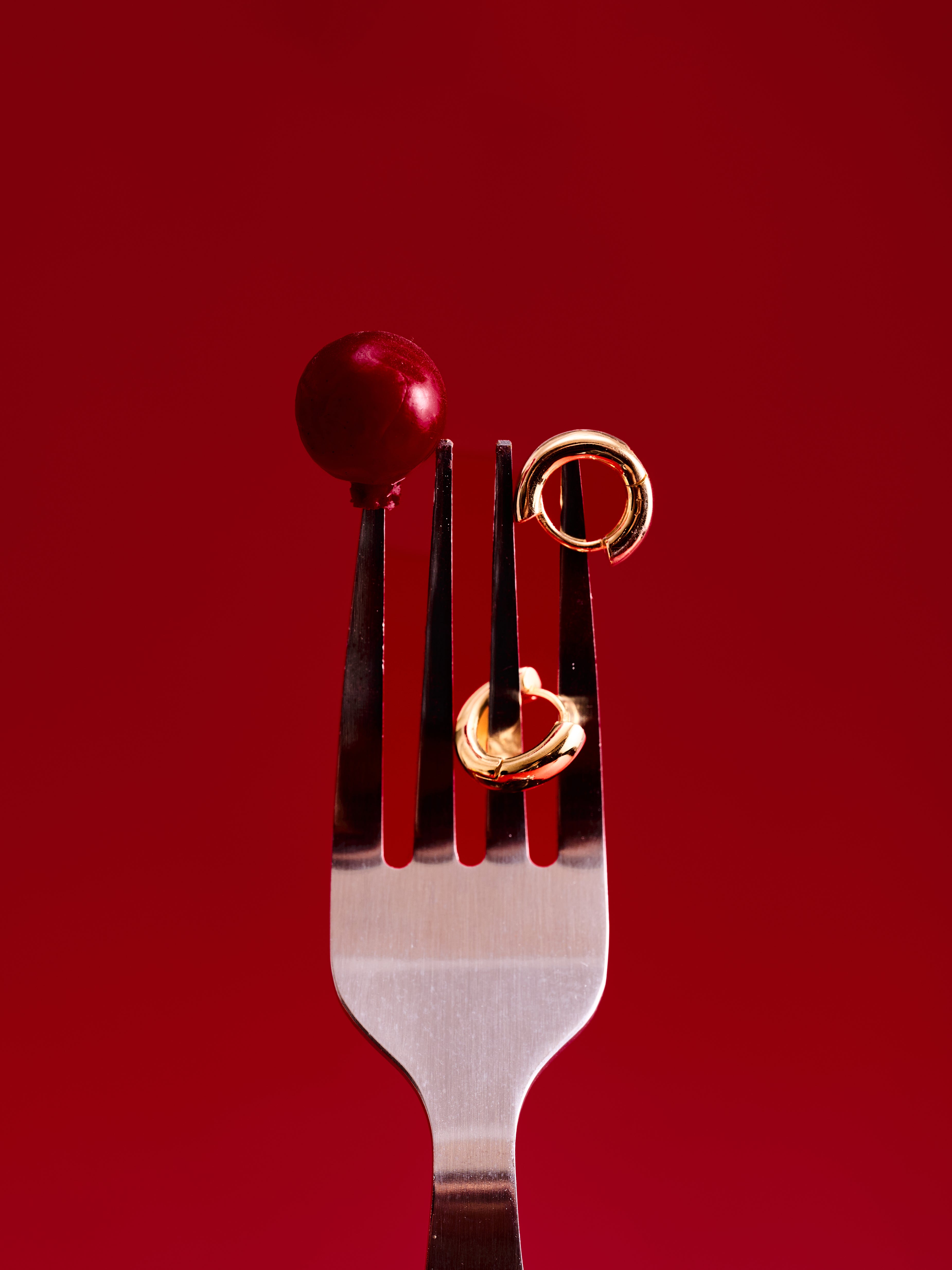 A silver fork holds a red cherry and two CAMELLIA Mia Hoops in 14K gold vermeil against a plain red background.