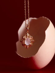 The CAMELLIA Capri Moonstone Necklace, featuring a vintage gold vermeil pendant with a luminous moonstone, is displayed in front of a cracked eggshell on a red background.