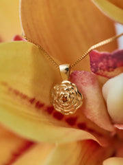 The CAMELLIA Elsa Birth Month Necklace shimmers as a gold vermeil pendant, gracefully resting against the petals of a yellow and red orchid.