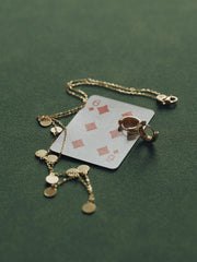 A six of diamonds playing card rests on a green surface, partially covered by a 14K gold vermeil chain necklace and CAMELLIA's hypoallergenic Mia Hoops earrings.