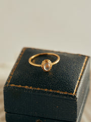 The CAMELLIA Eloise Moonstone Ring, a vintage-inspired piece with an oval-cut moonstone, is displayed on a black, textured jewelry box with worn edges.