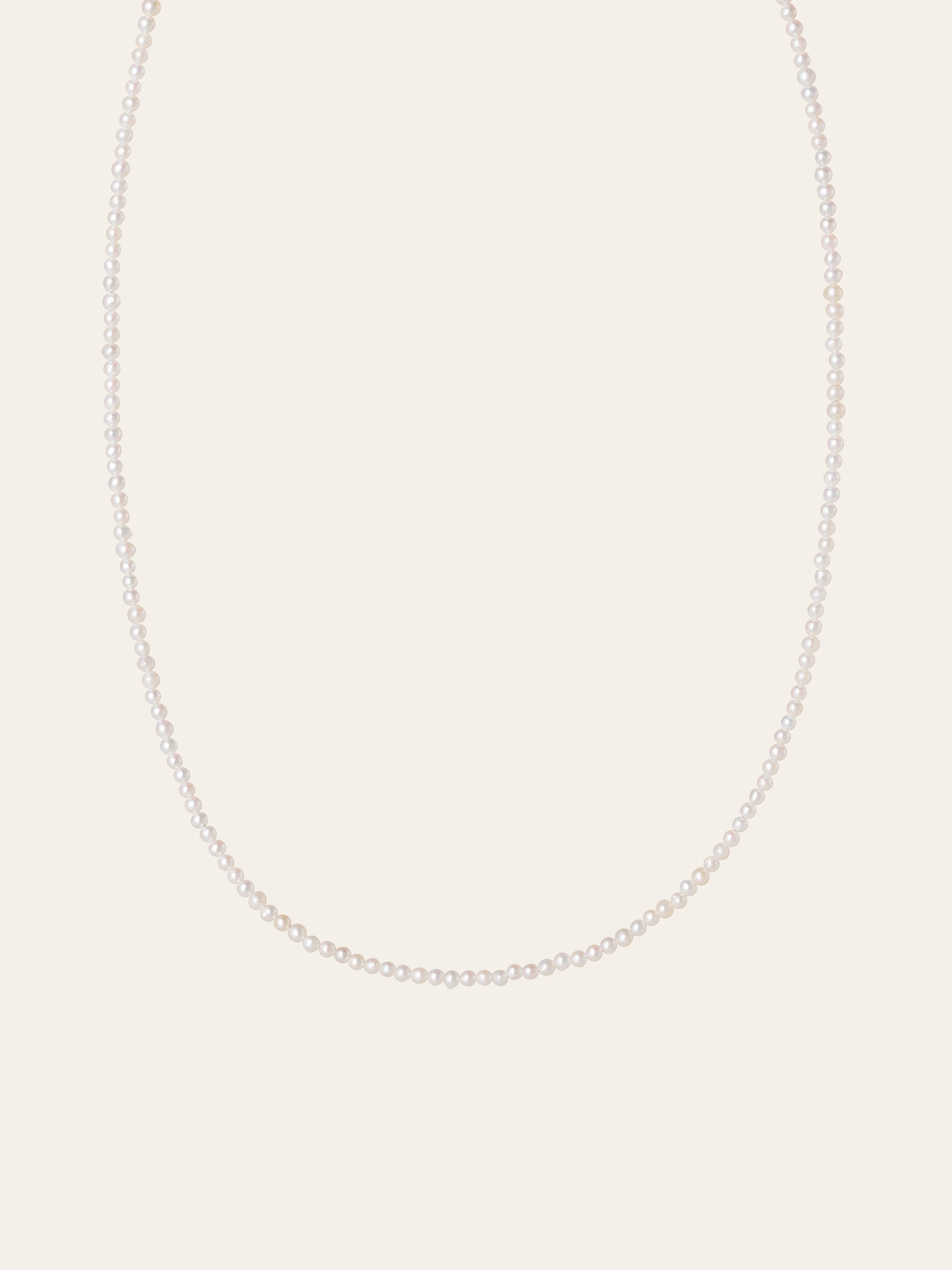The CAMELLIA Classic Pearl Strand Necklace features small white freshwater pearls, elegantly displayed against a plain, light-colored background.