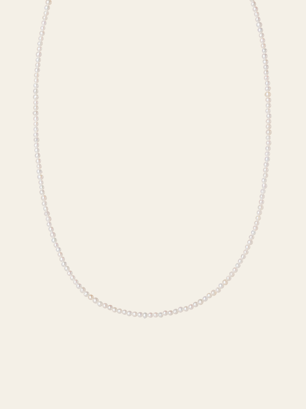 The CAMELLIA Classic Pearl Strand Necklace features small white freshwater pearls, elegantly displayed against a plain, light-colored background.