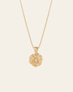 The Elsa Rose Pearl Necklace by CAMELLIA is a gold piece with a layered flower-shaped pendant, showcasing a central pearl, handcrafted in New York against a light background.