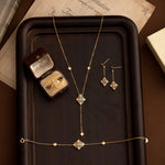 The CAMELLIA Aurielle Opal Jewelry Set, featuring a necklace, bracelet, earrings, and ring in a box, elegantly rests on a wooden tray. This hypoallergenic collection blends timeless design with exquisite gemstones for sensitive skin.