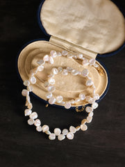 The CAMELLIA Petal Pearl Necklace, a baroque-style freshwater pearl piece, is showcased in an open cream-lined oval jewelry case on a dark surface.