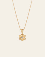 The CAMELLIA Elsa Cherry Aquamarine Necklace, a handcrafted gold piece with a star-shaped pendant and a central blue gemstone, elegantly displayed on a light background, radiates charm and sophistication.