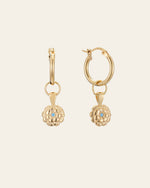 CAMELLIA's Elsa Marigold Tourmaline Earrings are gold hoops with dangling flower-shaped charms, each highlighting a small central blue tourmaline gemstone—October's birthstone—set against a plain background.